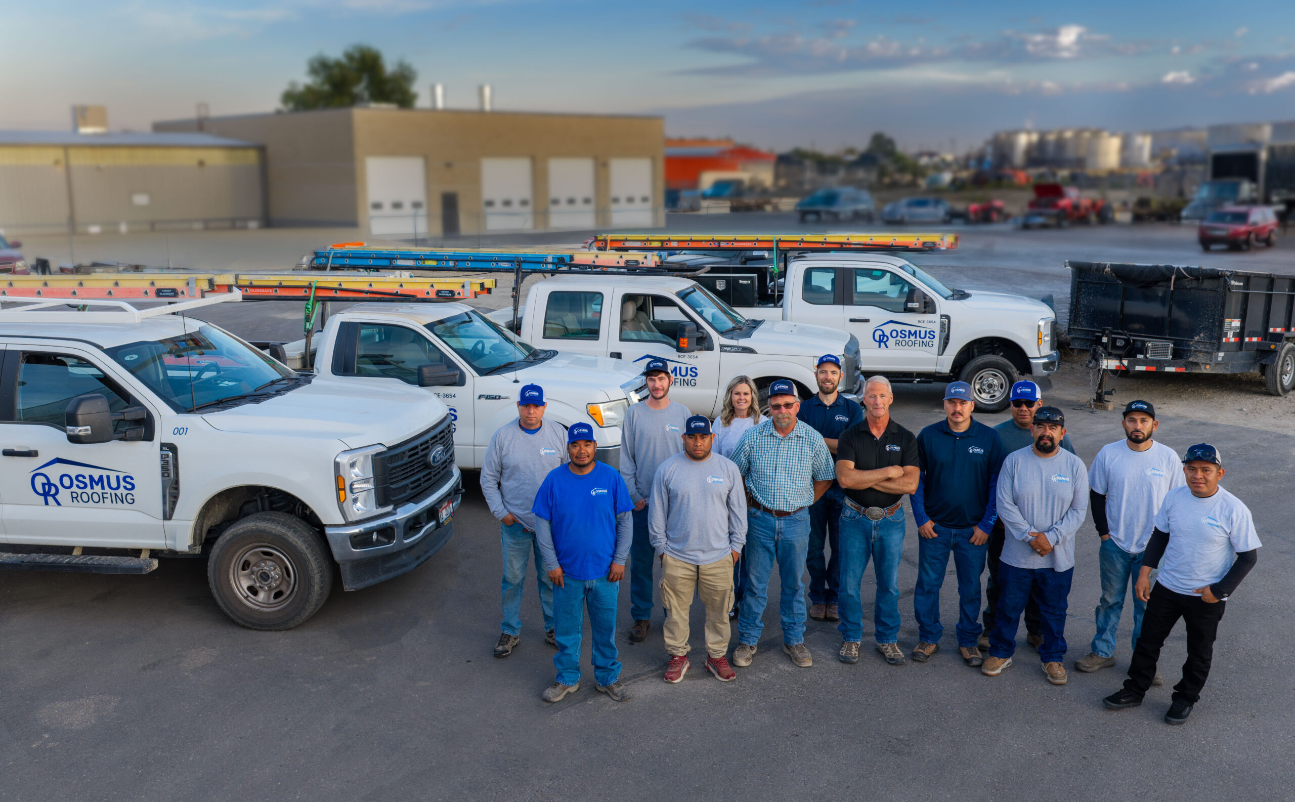 The Osmus Roofing team of staff and hard working people standing for a photo in their parking lot.